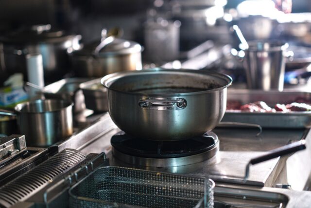 Bucătărie profesională cu echipamente din inox, cuptor și plită, pregătită pentru serviciu