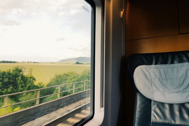 Peisaj de la țară văzut prin fereastra unui tren în mers, într-o zi senină