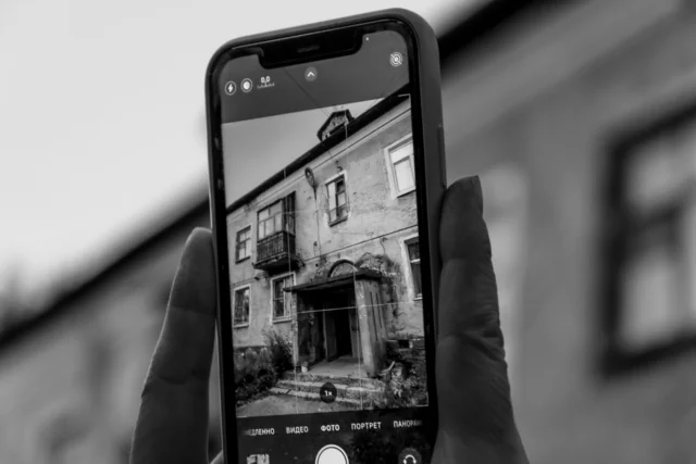 Mâinile unui om țin un telefon mai vechi, cu ecranul aprins pe setări, deasupra unei mese